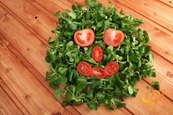 Smiley face made of red cherry tomato slices on green leafy bed on wooden surface