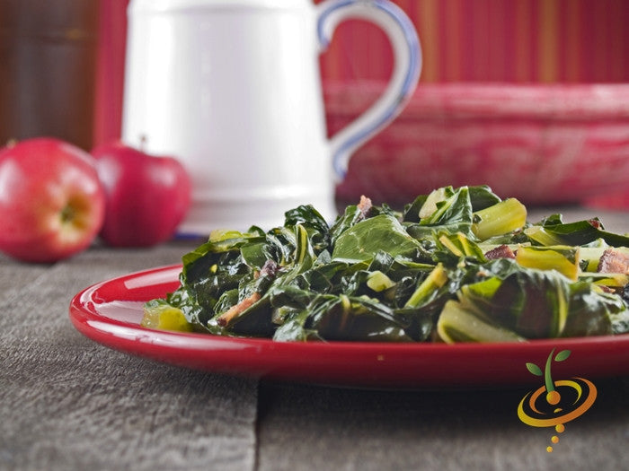 Cooked collard greens served on a red plate with apples and a cup in the background