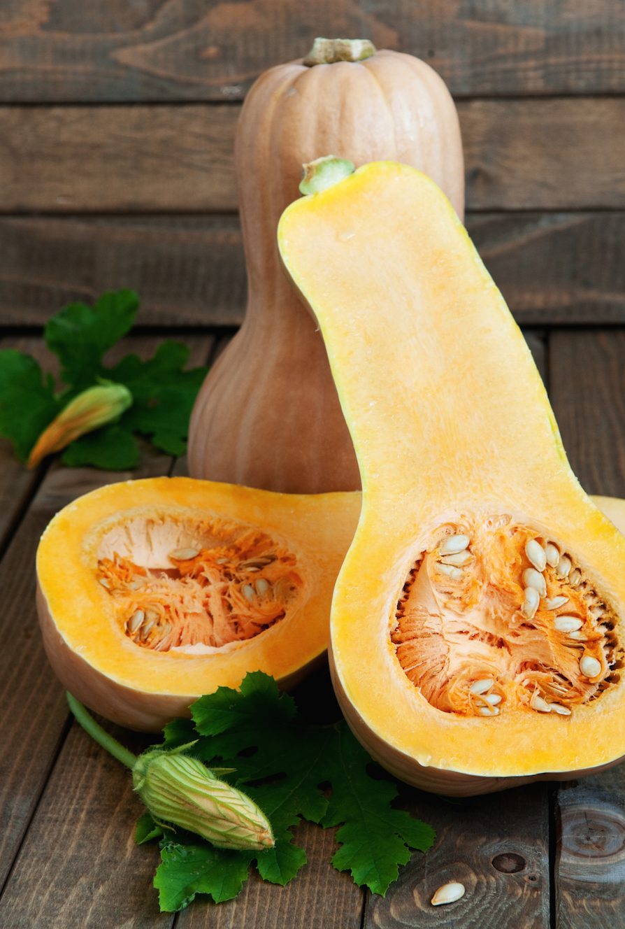 Waltham butternut winter squash with tan skin and deep orange interior cut open showing seeds on wooden background