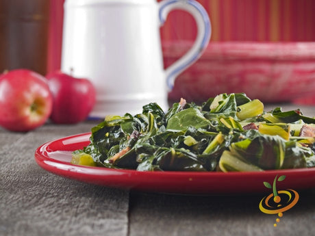Cooked collard greens served on a red plate with apples and a cup in the background